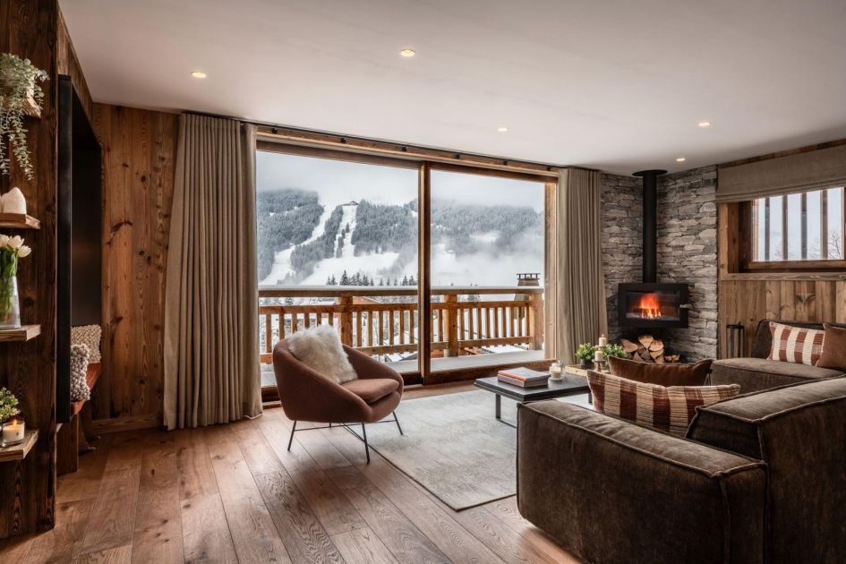 Living room of Chalet Tosca with a cosy corner wood-burning fire and snowy views out the window.