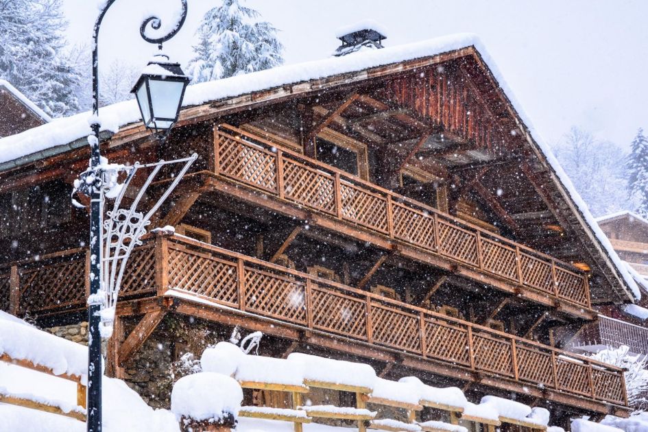 Wooden, chocolate-box exterior of Grange au Merle in the falling snow - a Châtel chalet perfect for skiing in the Portes du Soleil!