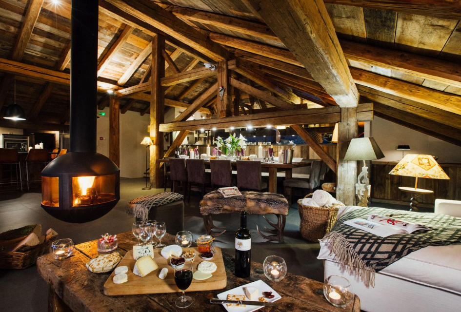 The bar area, floating fireplace, and seating of Chalet Debussy, a leading luxury eco chalet in Morzine, with cheese and wine spread for guest enjoyment.