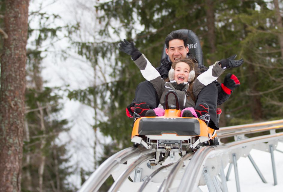 A father and daughter riding the Alpine Coaster at Planards in Chamonix, with trees in the background.