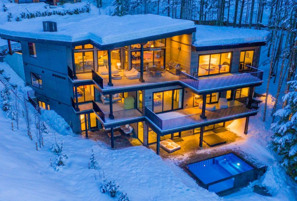 Chalet Solitude surrounded by snow, outdoor pool visible. Illuminated from the interior, this secluded luxury ski lodge in Canada is a fantastic choice for a ski trip to Whistler.