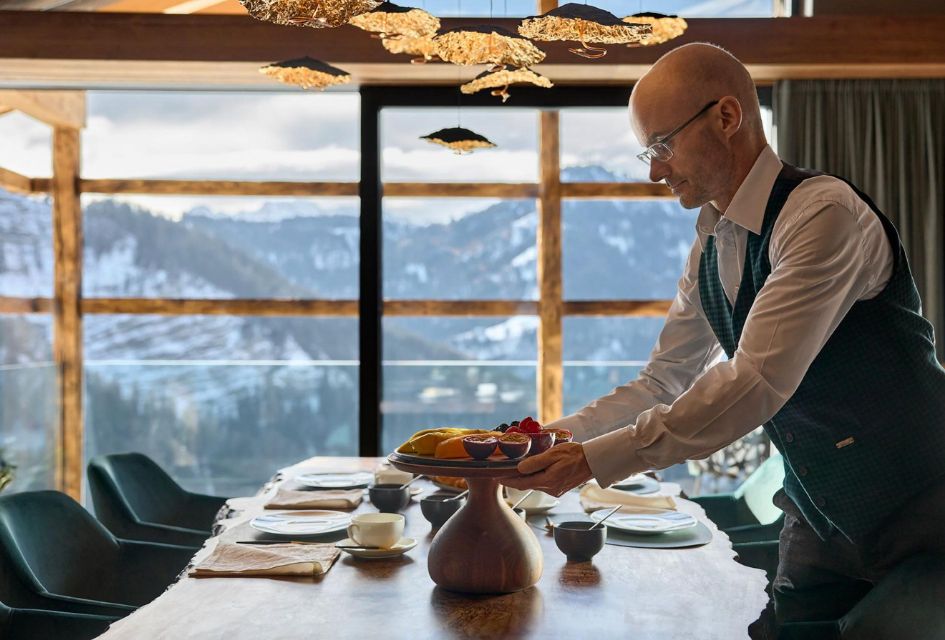 Server placing fruits on the dining table of Chalet Vilaiet, one of the top catered ski chalets in Italy. Surrounding windows showcase the snowy mountains of Ortisei