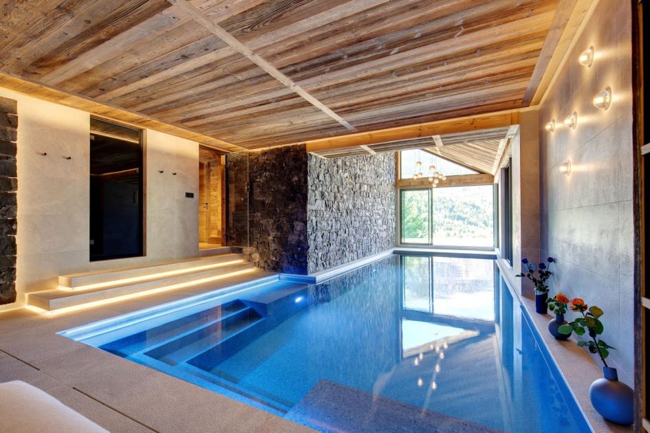 Chalet Ménor's indoor swimming pool is perfect for relaxing, featuring wooden and exposed stone to complement the spa-style tiles, with a window showing mountain views at the back.