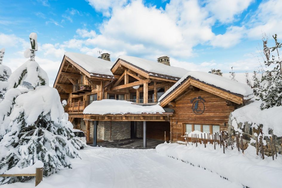 Surrounded by fir trees, Chalet Queen Mijane's wooden facade stands out amongst the snowy scenery adn blue skies.