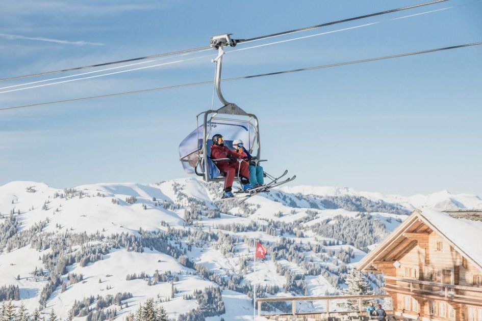 Two skiers on a cable car in Gstaad with a snowy background seen behind. With over 200km of pistes available, served by 42 ski lifts, luxury ski holidays in Gstaad have something for everyone!