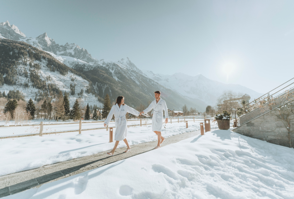 Two People walking hand in hand in front of the mountains at QC Terme spa in Chamonix.