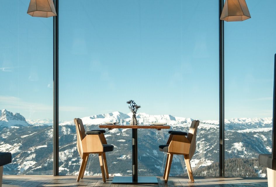 Table for two with a snowy mountain view through floor to ceiling windows in AlpINN, Brunico.  