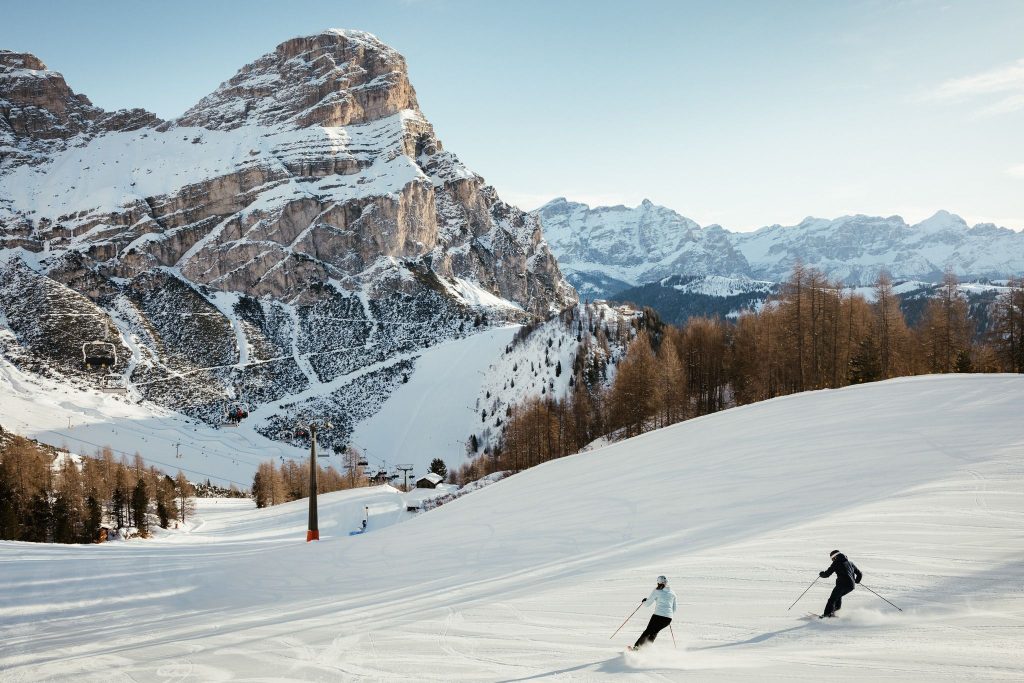 A couple skiing down the empty slopes in Alta Badia with a stunning Dolomiti views before them. 